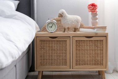Yatağın yanında çalar saati, dekorasyonu ve kitapları olan bir komodin.