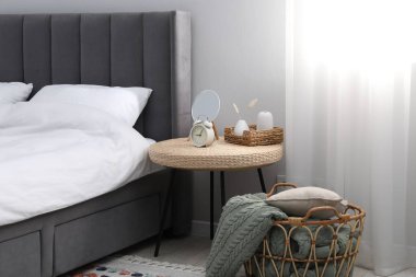 Yan masada ayna, çalar saat ve yatağın yanında dekor var.