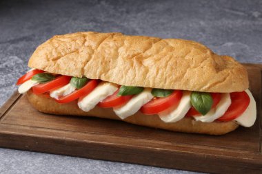 Mozarella peynirli, domatesli ve fesleğenli lezzetli sandviç. Gri desenli masa, yakın plan.