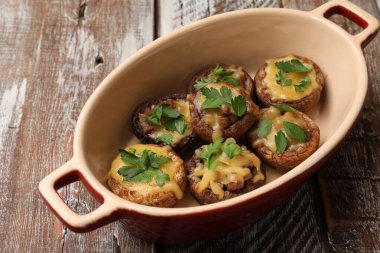 Eritilmiş peynirli ve maydanozlu lezzetli mantarlar ahşap masa üzerinde, yakın plan.