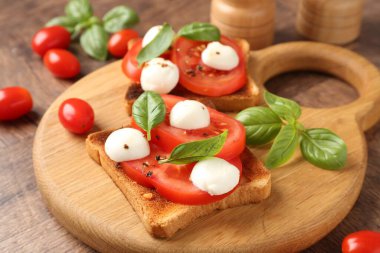 Mozarella peynirli, domatesli ve ahşap masadaki fesleğenli lezzetli sandviçler.