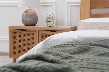 Yatağın yanında lamba ve çalar saat olan komodinin yanında.