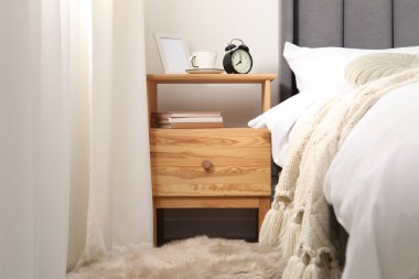 Yatağın yanında çalar saati, kahvesi ve çerçevesi olan bir komodin.