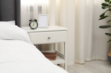 Alarm saati ve yatağın yanındaki çerçeveli komodinin yanında.