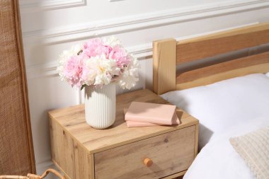 Yatağın yanında kitaplar ve çiçekler olan komodin.