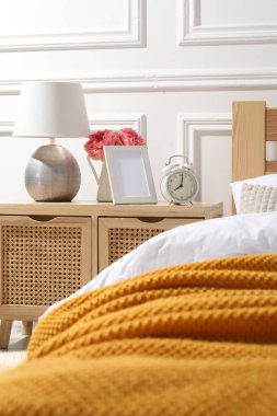 İçinde lamba, çalar saat ve yatağın yanında çiçekler olan komodin.