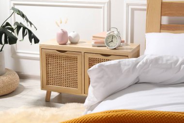 Yatağın yanında çalar saati, kitapları ve dekorasyonu olan bir komodin.