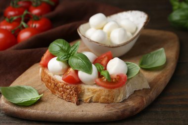 Mozarella peynirli, domatesli ve ahşap masadaki fesleğenli lezzetli sandviç.