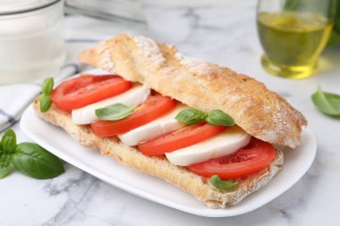 Mozarella peynirli, domatesli ve fesleğenli lezzetli sandviç beyaz mermer masada, yakın plan.