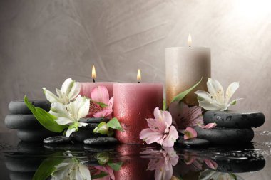 Yanan mumlar, spa taşları ve ıslak siyah masada güzel çiçekler.