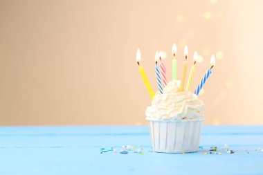 Kekin içinde mum yakmak ve açık mavi masaya serpiştirmek bej arka planda bulanık ışıklarla