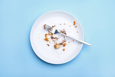 Açık mavi arka planda kırıntılı, kremalı ve çatallı kirli tabak.