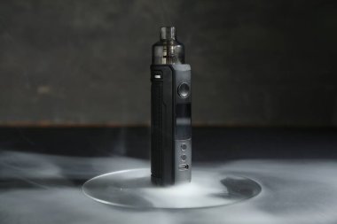 Gri arkaplana karşı siyah masada dumanlı bir elektronik sigara aleti, yakın plan.