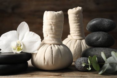 Ahşap masada bitkisel poşetler ve spa taşlarıyla kompozisyon, yakın plan.