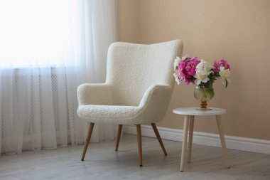 Rahat koltuk ve masa. Kapalı mekanda bir vazo çiçek var.