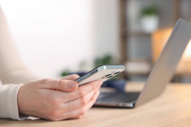 Ahşap masada modern akıllı telefon kullanan kadın, yakın plan.