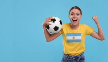 Yanağında Arjantin bayrakları ve açık mavi arka planda futbol topu tutan tişörtü olan heyecanlı bir taraftar. Metin için alanı olan pankart tasarımı