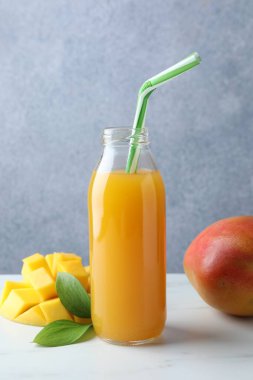 Cam şişede lezzetli mango suyu, taze meyve ve beyaz mermer masada yeşil yapraklar.