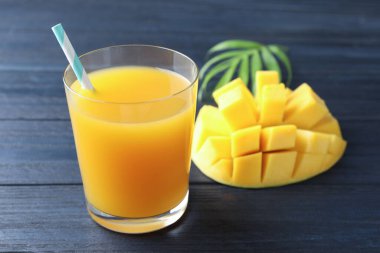 Bardakta lezzetli mango suyu, taze meyve ve ahşap masada yeşil yapraklar, yakın plan.