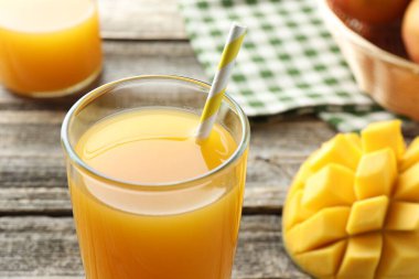 Bardakta lezzetli mango suyu ve ahşap masada taze meyve, yakın plan.