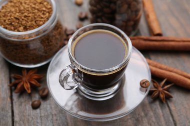 Bir fincan aromatik kahve, fasulye, hazır toz ve baharatlar ahşap masada, yakın plan.