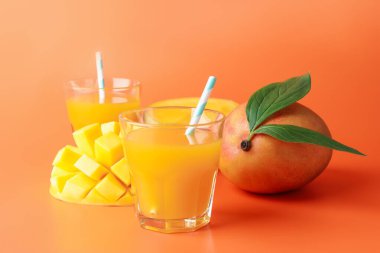 Bardakta lezzetli mango suyu ve turuncu arka planda taze meyve.