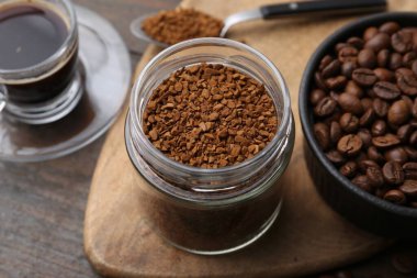 Cam kavanozdaki anlık kahve, sıcak içecek ve ahşap masada fasulye, yakın plan.