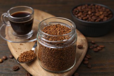 Cam kavanozdaki anlık kahve, sıcak içecek ve ahşap masada fasulye, yakın plan.