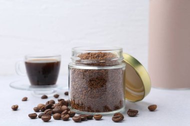 Cam kavanozdaki anlık kahve, fasulye ve sıcak içecek açık gri masada, yakın plan.