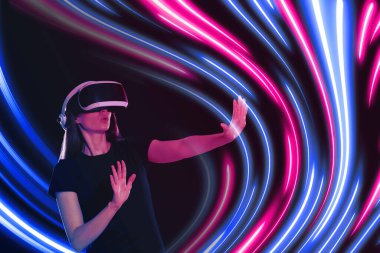 Karanlık arka planda sanal gerçeklik kulaklığı kullanan bir kadın. Etrafında parlak neon çizgiler var.