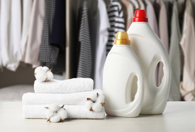 Kumaş yumuşatıcı, çamaşır deterjanı, havlular ve pamuk çiçekleri masadaki gardıroba karşı.