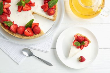 Çilekli nefis peynirli kek, nane şekeri ve beyaz ahşap masa üzerinde çay.