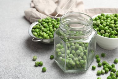 Açık gri masada taze bezelye ve turşu kavanozu, yakın plan.