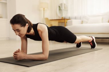 Genç bir kadın evdeki fitness paspası üzerinde tahta egzersizi yapıyor. Spor ve sağlıklı yaşam tarzı