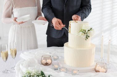 Damat düğün pastasından bir parça alırken gelin tabakları içeride tutuyor, yakın plan.