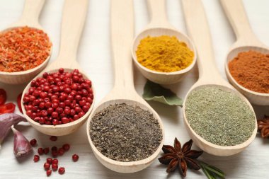 Beyaz ahşap masadaki kaşıklarda farklı aromatik baharatlar, yakın plan.
