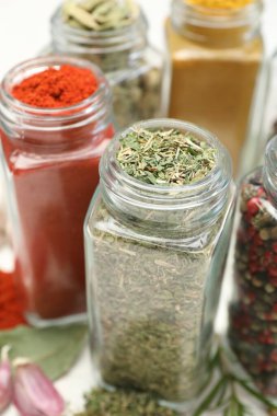 Beyaz masadaki kavanozlarda farklı aromatik baharatlar, yakın plan.