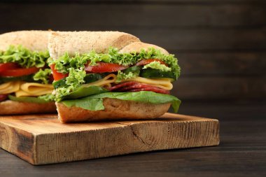 Lezzetli baget sandviç parçaları füme sosis, peynir ve sebzeler ahşap masada, yakın plan.