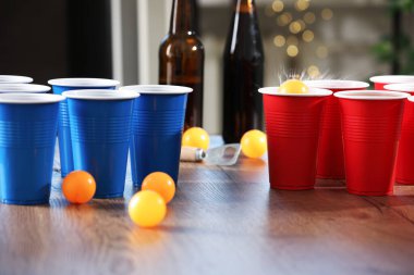 Bira pong oyunu. İçkili plastik bardaklar ve toplar ahşap masada, yakın plan.