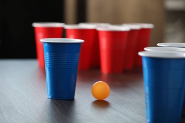 Bira pong oyunu. İçkili plastik bardaklar ve tahta masada top, yakın plan.