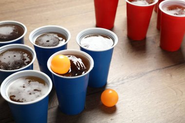 Bira pong oyunu. İçkili plastik bardaklar ve toplar ahşap masada, yakın plan. Metin için boşluk