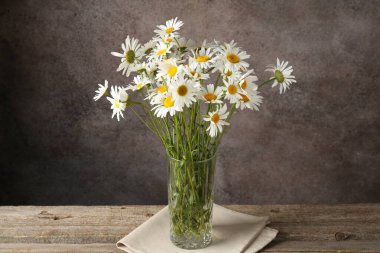 Tahta masadaki vazoda, kahverengi desenli arka planda birçok güzel papatya çiçeği, yakın plan.