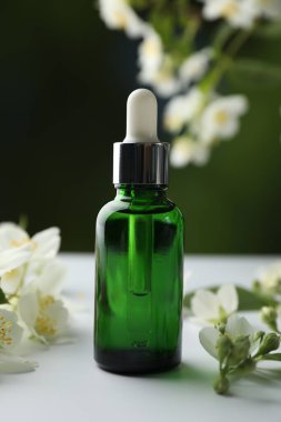 Temel yağ ve yasemin çiçekleri beyaz masada bulanık arka planda, yakın plan