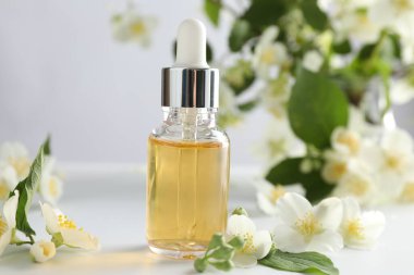 Temel yağ ve güzel yasemin çiçekleri beyaz masada, yakın plan.