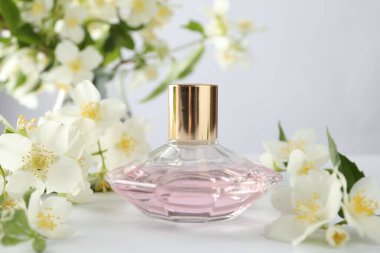 Beyaz masada bir şişe parfüm ve yasemin çiçeği, yakın plan.