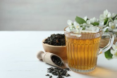 Cam bardakta Aromatik yasemin çayı, beyaz ahşap masada çiçekler ve kuru yapraklar, yakın plan. Metin için boşluk