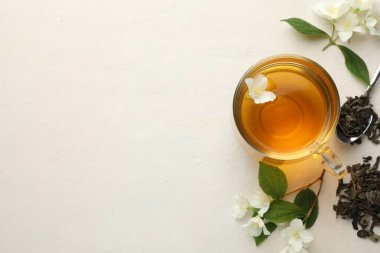 Cam bardakta Aromatik yasemin çayı, beyaz masada çiçekler ve yapraklar, düz uzanmış. Metin için boşluk