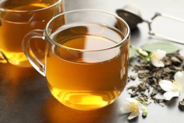 Cam fincanlarda yasemin çayı, gri masada bira ve çiçekler, yakın plan.