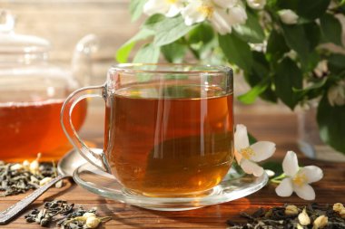 Aromatik yasemin çayı cam bardakta, çaydanlık, demlik ve çiçekler ahşap masada, yakın plan.