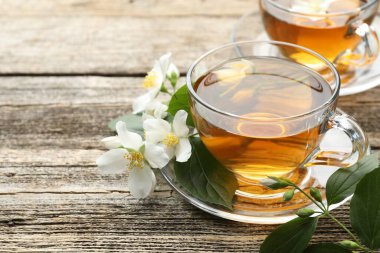 Cam bardaklarda yasemin çayı, ahşap masada çiçekler ve yeşil yapraklar, yakın plan. Metin için boşluk